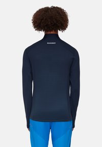 Langearmige navy performance shirt met een hoge kraag, gestructureerd oppervlak en het "Mammut"-logo op de achterkant, gecombineerd met blauwe sportbroeken.
