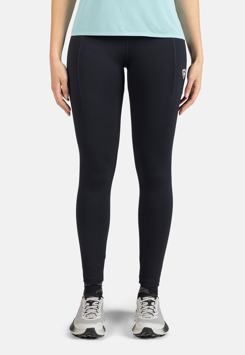 Schwarze Leggings aus dehnbarem Stoff mit seitlichen Nähten und einem Logopatch, kombiniert mit weißen und grauen Sportschuhen.