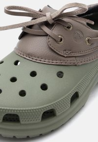 Πράσινο και καφέ παπούτσι Crocs με οπές αερισμού, υφασμένο πέλμα, δερμάτινο περιλαίμιο και δεμένα δερμάτινα κορδόνια.