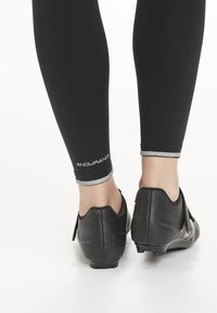 Black cycling leggings with gray accents at the ankles, paired with black cycling shoes featuring a smooth finish and fastening straps.