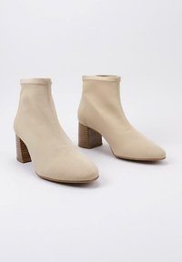 Botas de tobillo beige hechas de tela con una textura suave, punta afilada y un tacón de madera grueso con ranuras verticales.