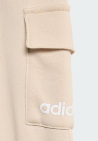 Beżowa bluza z rękawem z kieszonką naszywaną i białym logo "adidas" na mankiecie. Gładka tekstura o jednolitym wzorze dzianiny.