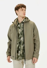 Wasserabweisende, olivgrüne Jacke mit Reißverschluss und verstellbarem Kapuzen über einem gemusterten grünen Hemd. Leichte Stoffqualität; lässiger Schnitt.