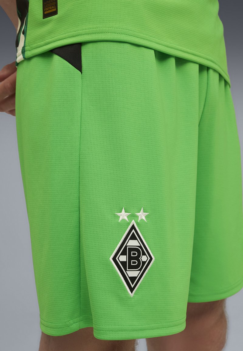 Zelene športne kratke hlače iz zračnega materiala, z mrežno strukturo, stranskimi žepi in črno-belo logo s dvema zvezdama.