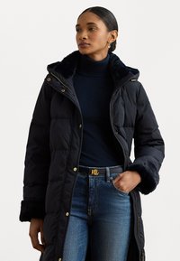 Dlhý puffer kabát v tmavomodrej farbe s umelou ko�žušinou na golieri a manžetách. Obsahuje zlaté kovanie, zips a lichotivý priliehavý strih.