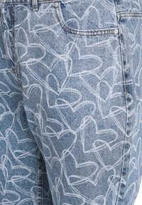 Gai zils džinsu bikses ar baltiem sirds rakstiem visā virsmā, klasiskā piecu kabatu dizainā un redzamām šuvju detaļām.