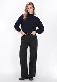 Marineblauwe geribbelde trui met hoge hals, oversized mouwen, gecombineerd met hoge taille zwarte wijde jeans en zwarte enkellaarsjes.