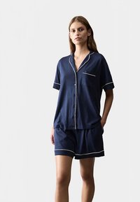 Marineblåt kortærmet pyjamasæt i letvævet stof, med en skjorte med knapper og brystlomme samt kontrasterende hvide kanter på ærmer og shorts.