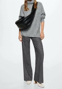 Szary sweter z prążkowanym golfem, czarna skórzana torba na ramię, szare spodnie w dzwony, kremowe buty na słupku o gładkiej fakturze.