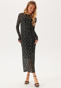 Sort, langærmet kjole med blomstermønster, skrådesignet og gennemsigtig tekstur. Båret med sorte strophæle.