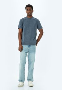 Grå bomullströja med rund halsringning, korta ärmar och urblekt textur. Matchas med ljusblå denimjeans och vita sneakers.