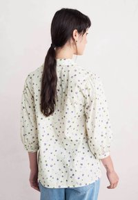 Vit blus med gröna och lila prickar, långa puffärm och knäppning bak. Mjuk tyg med en något strukturerad yta.