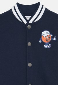 Marineblauwe sweatshirt met een gestructureerd oppervlak, gestreepte ribkraag, zilveren drukknoopjes en een grafische cartoon-basketballfiguur.