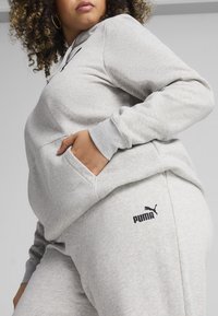 Grau Hoodie und Jogginghose aus weichem Material, ausgestattet mit einer Kängurutasche und schwarzem Puma-Logo auf der linken Seite.
