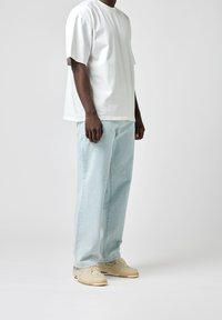 Biała bawełniana koszulka z krótkim rękawem, zestawiona z jasnoniebieskimi dżinsami i beżowymi tenisówkami z subtelnymi akcentami i fakturowanym wykończeniem.