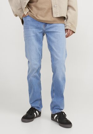 Jeans de denim azul claro con corte recto, que cuentan con cinco bolsillos y un ligero desgaste. Combinados con zapatillas negras y una chaqueta beige.