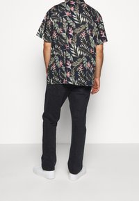 Kortärmad, mörkblommig skjorta med gröna blad och rosa blommor, kombinerad med svarta byxor och vita sneakers. Avspänd, avslappnad passform.