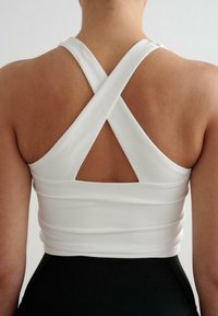 Fehér sport crop top keresztbe csatolt pántokkal és kivágott részlettel a háton, rugalmas anyagból készült, testhez simuló és bordás textúrával.