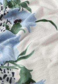Tessuto floreale con fiori blu chiaro e foglie verdi su uno sfondo bianco, che mostra un aspetto soffice e strutturato.