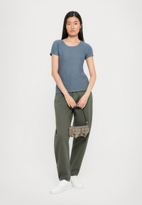 Blue ribbed short-sleeve top, olive green wide-leg pants, white sneakers, grey handbag with buckle accents, set against a plain background.