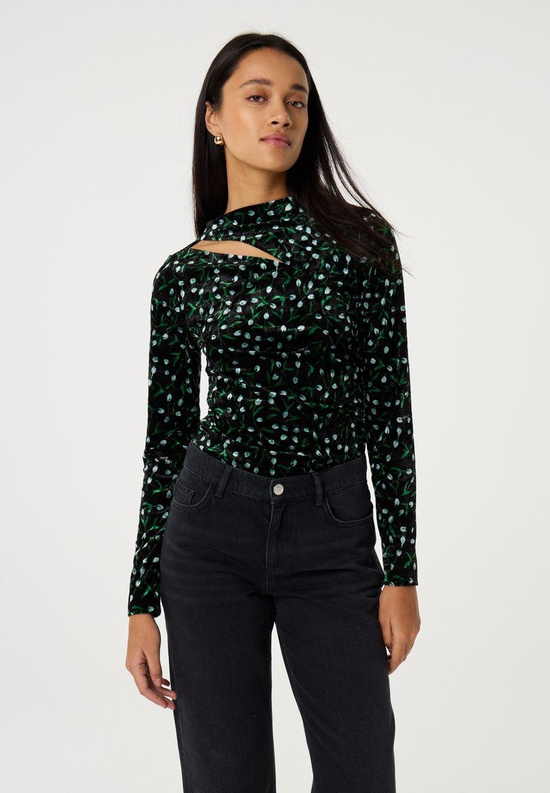 Zwarte fluwelen top met lange mouwen, voorzien van een groen en witte bloemenprint, met een uitgesneden halsdetail en een slim fit, gecombineerd met zwarte jeans.