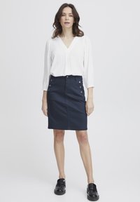 Jūras zilās krāsas denima svārki ar priekšējiem pogām, šaura piegriezuma un līdz ceļiem; apvienoti ar balto, vieglo, garo piedurkņu blūzi ar V veida kakla izgriezumu.