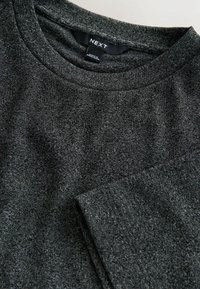 Dunkelgraues Langarmshirt aus einem weichen, strukturierten Stoff. Rundhalsausschnitt mit einem Etikett, das "NEXT" zeigt. Einfaches, unverziertes Design.