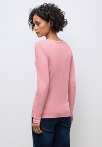 Roze lange mouwen top van zachte katoen met een ronde hals en aansluitende mouwen, gecombineerd met donkerblauwe jeans, gezien vanuit de achterkant.