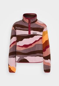 Sudadera de felpa con rayas onduladas abstractas en marrón, rosa, rojo, naranja y púrpura, con media cremallera y pequeño logo de Converse en el pecho.