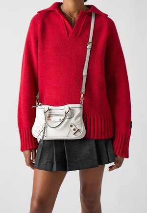 Weiße Handtasche aus Kroko-Prägung mit silbernen Beschlägen, kombiniert mit einem roten Strickpullover und einem schwarzen plissierten Rock. Langer verstellbarer Riemen.