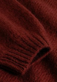 Gestrickter Pullover aus tief bordeauxroter Wolle. Verfügt über eine gerippte Manschette und einen weichen, strukturierten Stoff mit einem leicht flauschigen Aussehen.