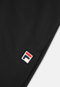 Czarna tkanina o teksturowanej powierzchni posiada łatkę logo FILA w kolorach czerwonym, białym i niebieskim na białym tle.