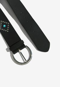 Fekete bőr öv türkiz színű drágakő díszítéssel és ezüst színű kerek csattal. Díszvarrásokkal és több állítható lyukkal rendelkezik.