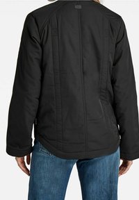 Czarna ocieplane kurtka o miękkiej teksturze, z zaokrąglonym dołem, widocznymi szwami i metką z tyłu. W połączeniu z niebieskimi dżinsami.