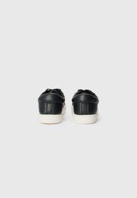 Sorte lærersneakers med hvit gummisåle, med avrundte hæler og kontrasterende sømmer på baksiden. Klassisk lavtoppsdesign.