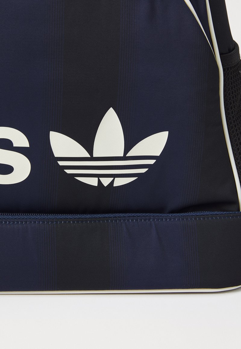 Sac de sport bleu marine avec une surface texturée, arborant un logo Adidas blanc bien visible et un accent crème contrastant le long de la fermeture éclair.
