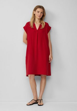 Rotes, knielanges Kleid aus strukturiertem Stoff mit kurzen Ärmeln und V-Ausschnitt. Kombiniert mit schwarzen, strappy Sandalen.