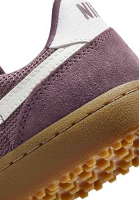 Close-up of a purple suede and mesh sneaker heel with white leather detail, brown textured sole, and partial Nike logo.