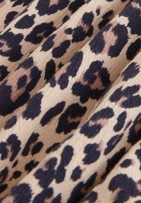 Tkanina z leopardjim vzorcem z velikimi črnimi in rjavimi lisami na bež podlagi, s mehko, teksturirano površino. Gubast videz.