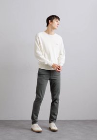 Hanorac alb cu un logo roșu mic, pantaloni gri și adidași albi cu tălpi bej. Design simplu și croială lejeră.