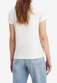 Camiseta blanca de manga corta hecha de suave algodón, con un corte relajado y dobladillo ligeramente redondeado, combinada con jeans de mezclilla azul claro.