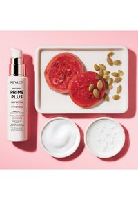 Botella de Revlon Photoready Prime Plus, blanca con acentos plateados. Presenta dos rodajas de tomate rojo, semillas verdes, una sustancia cremosa blanca y una crema texturizada de color gris claro.