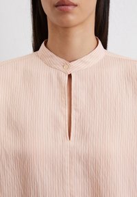 Helles rosa, kragenbluse mit vertikalen weißen Streifen, ausgestattet mit einer Knopfverschluss und einem kleinen Ausschnitt-Detail am Halsausschnitt.