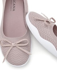 Zapatillas de color rosa claro, tejidas y tipo slip-on, con una superficie texturizada, que presentan un lazo decorativo en la parte frontal y una suela de goma blanca.