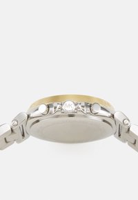 Orologio in acciaio inossidabile argentato con una ghiera dorata. Presenta tre pulsanti a corona e un bracciale a maglie texturizzato. Il retro è liscio e privo di segni.
