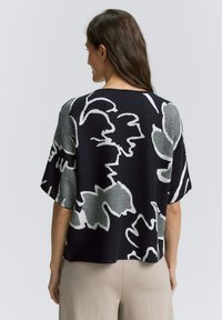 Czarny dzianinowy top o luźnym, pudełkowym kroju, z dużym białym i szarym wzorem kwiatowym. Krótkie, szerokie rękawy i okrągły dekolt.