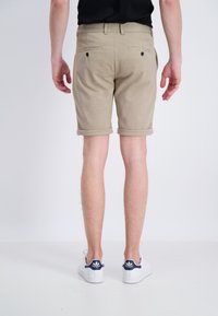 Pantaloni corti beige con risvolti, due tasche posteriori con bottoni neri, abbinati a sneakers bianche con dettagli blu navy.