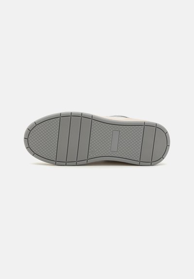 Gray rubber sneaker sole with horizontal grooves, textured surface, and a rectangular logo in the midsole. Features a sturdy design for traction.