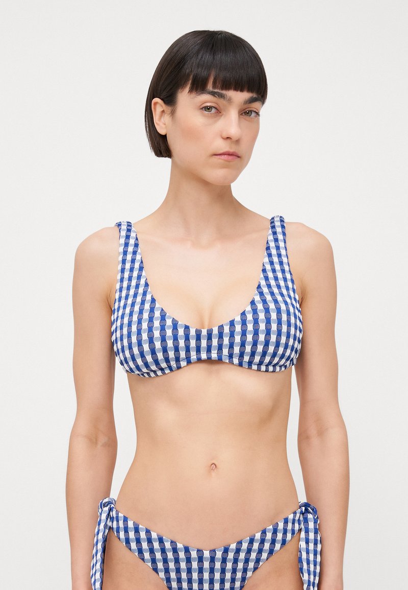 Blå og hvit gingham bikini med scoop halslinje, tykke skulderstropper og justerbare knytedetaljer i bunnen. Glatt stofftekstur.