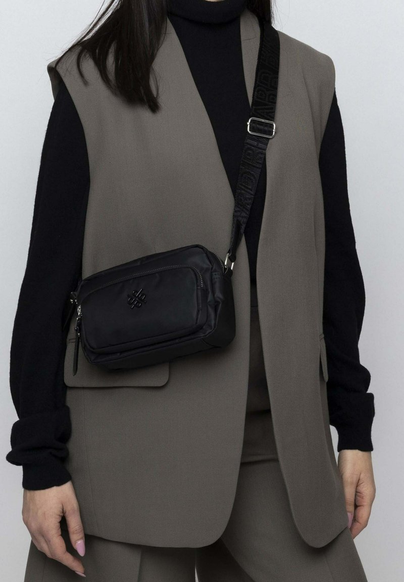 Schwarze Umhängetasche aus Nylon; verfügt über ein Reißverschlussfach, ein Logo und einen verstellbaren Riemen mit einem strukturierten Muster.